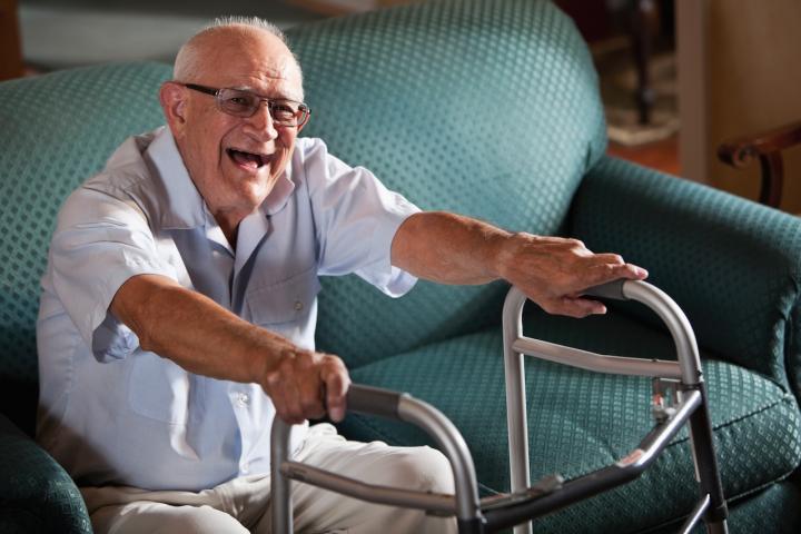 Senior man (80s) laughing, getting up from couch, using walker
